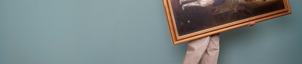A person carrying a large framed picture past a plain wall while moving house